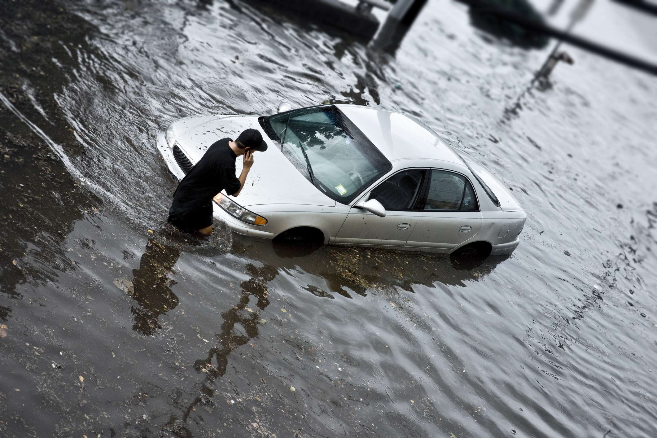 un homme au téléphone se tenant à côté de sa voiture inondée